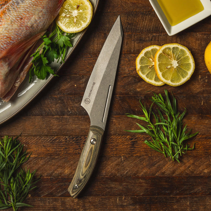 The 6.5 inch Carbon Chef's Knife shown lying next to a platter of fish with lemon slices and herbs