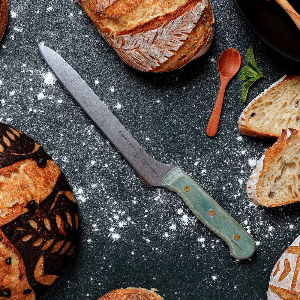 Messermeister Custom Blue Scalloped Offset Knife - 8" surrounded by sourdough bread on a black surface