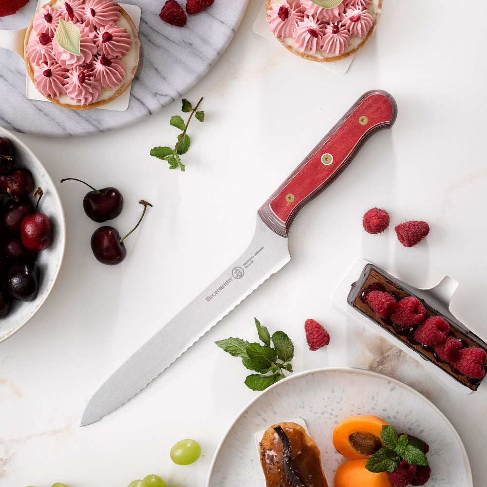 8-inch Messermeister Custom Red scalloped offset knife on white background beside pastries and cherries, showing serrated stainless blade and red ergonomic handle