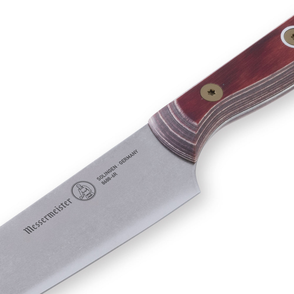 Close-up of the heel of a 6-inch Messermeister Custom Red utility knife, showing the thick base of the polished stainless steel blade meeting the red ergonomic handle