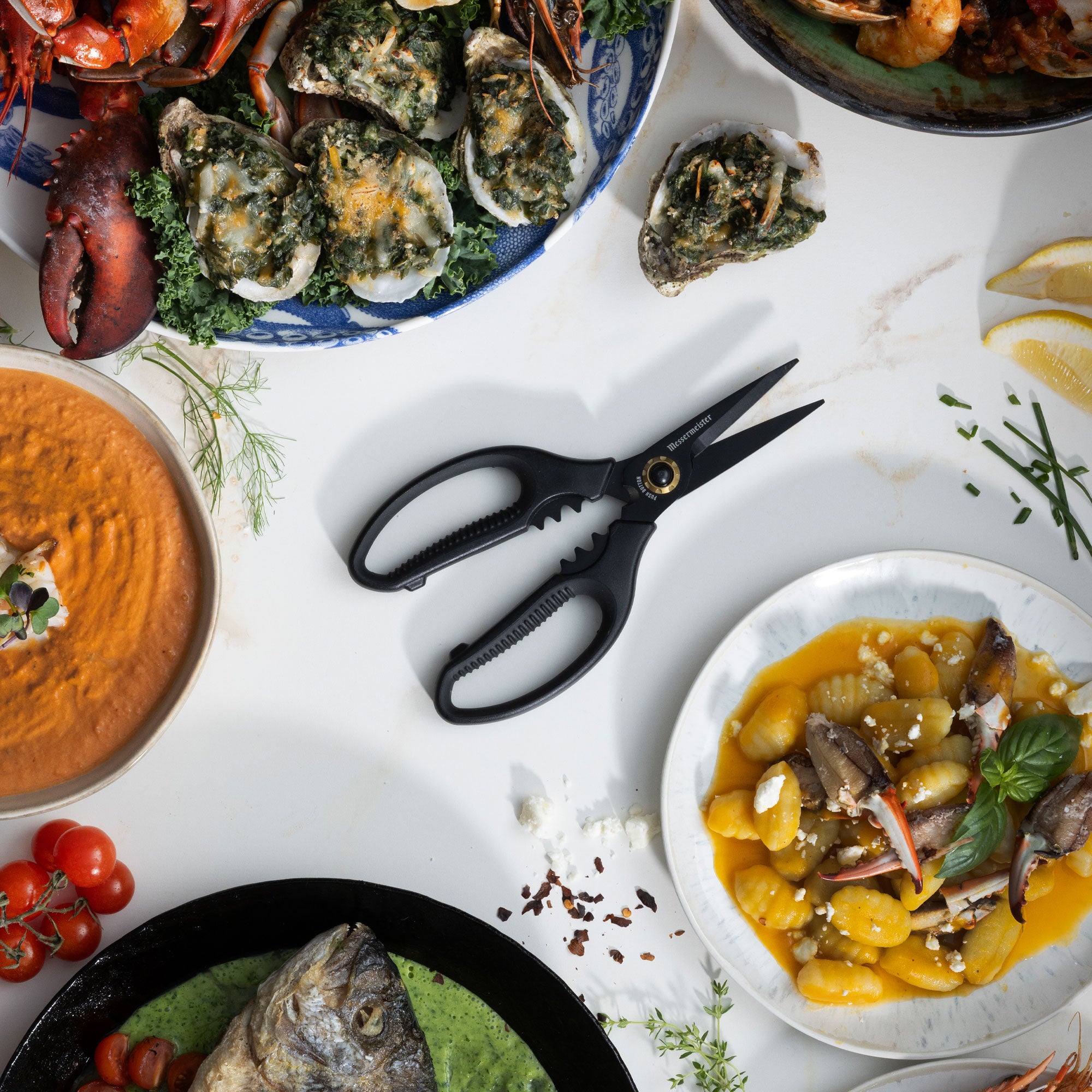 Esther Choi 7-inch push button take-apart precision shears resting on a white table between assorted seafood dishes, featuring stainless steel blades and ergonomic handles for precise kitchen prep and seafood preparation