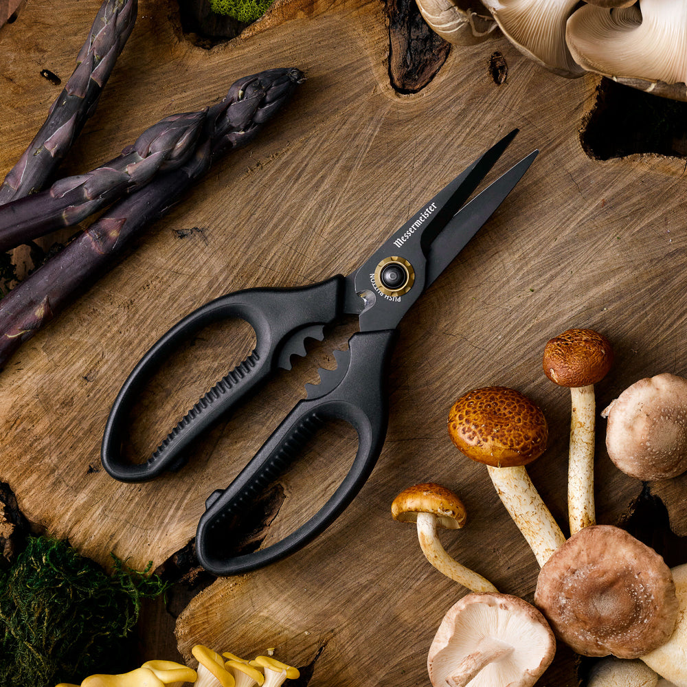 All black Messermeister Esther Choi Push Button Precision Shears with foraged mushrooms and  purple asparagus on a wood surface