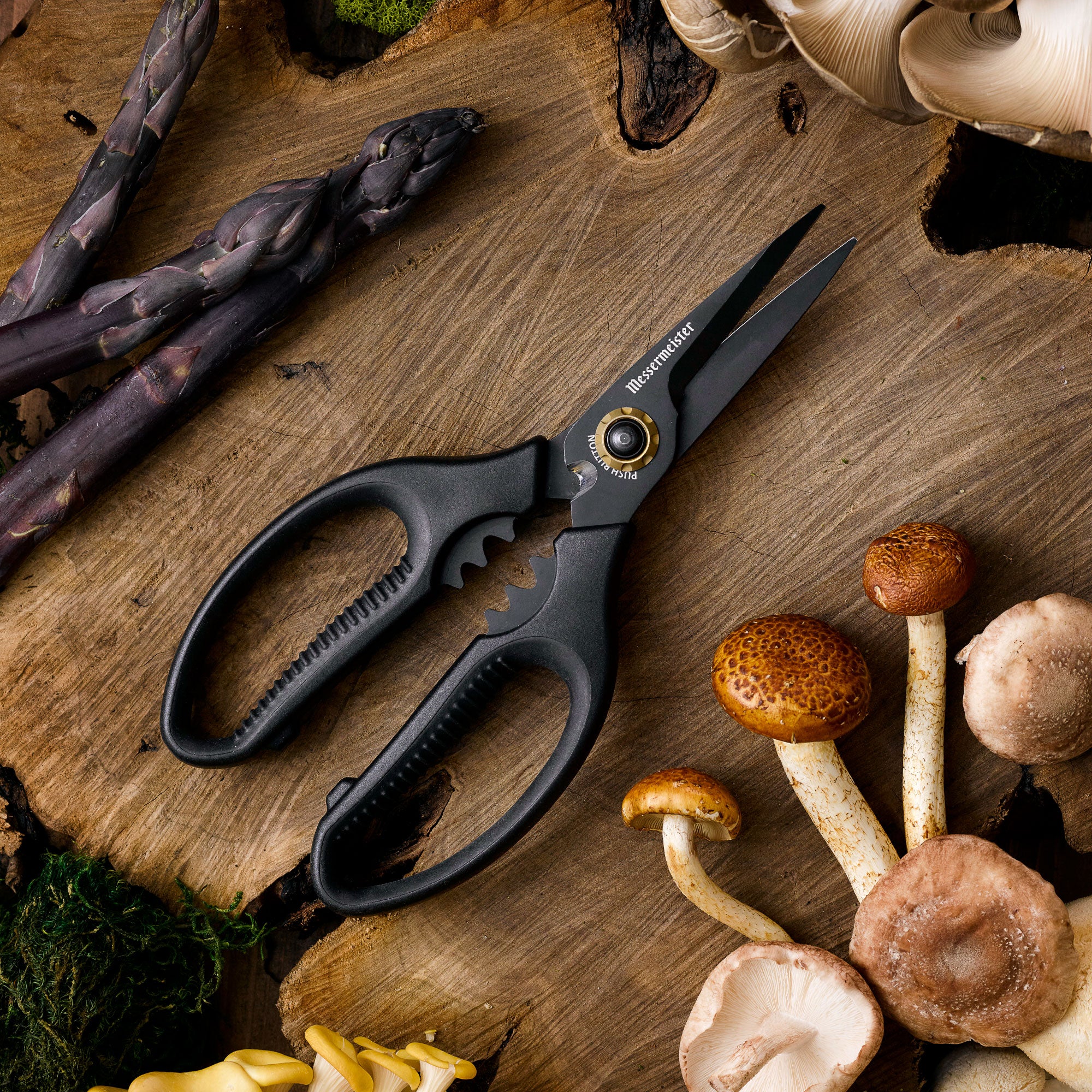 All black Messermeister Esther Choi Push Button Precision Shears with foraged mushrooms and  purple asparagus on a wood surface