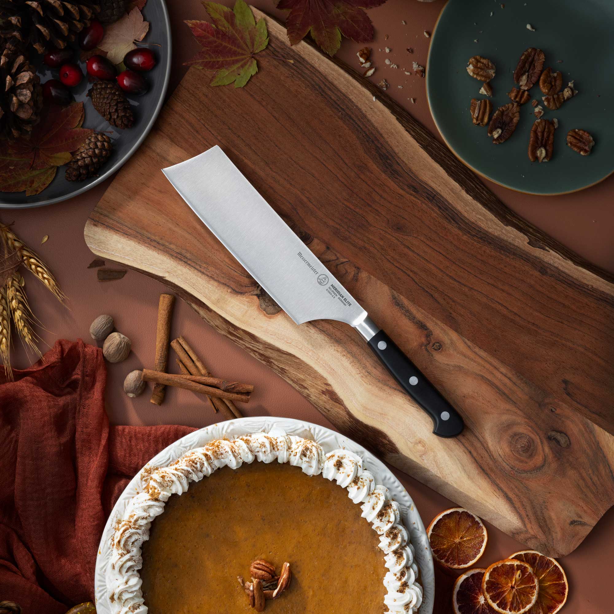 Pumpkin pie on a wooden cutting board with a Messermeister Meridian Elite Nakiri knife, surrounded by autumn decorations.