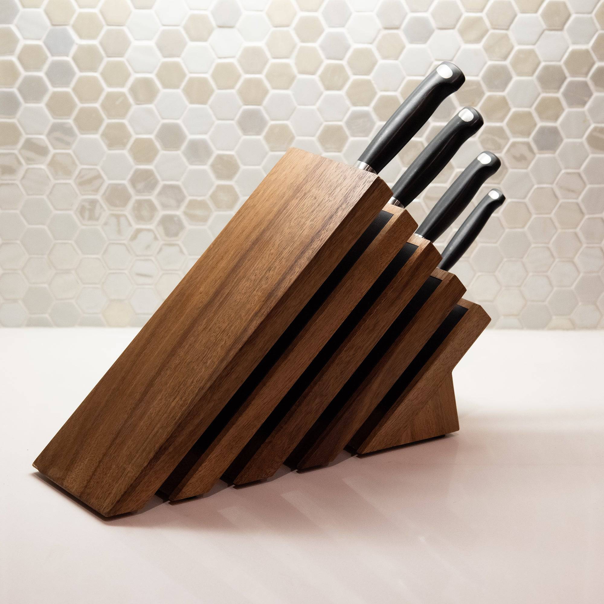 Messermeister Next Level Magnetic Knife Block with a single black handles knife stored on each of the 4 slots. Sitting on a white counter and octagon backsplash. 