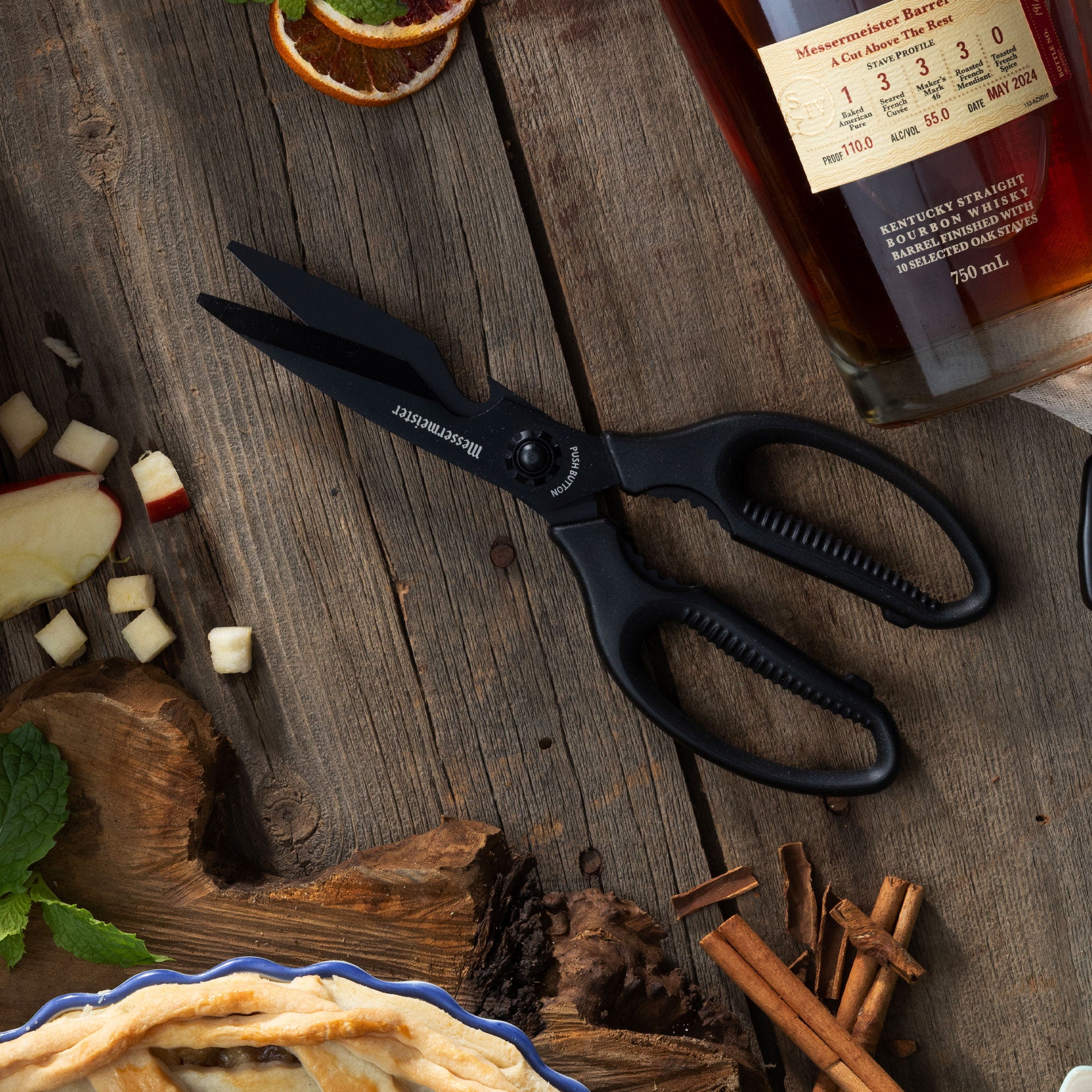 All black Messermeister Push Button Shears Shears with pie crust, cinnamon sticks, diced apple and a bottle of bourbon