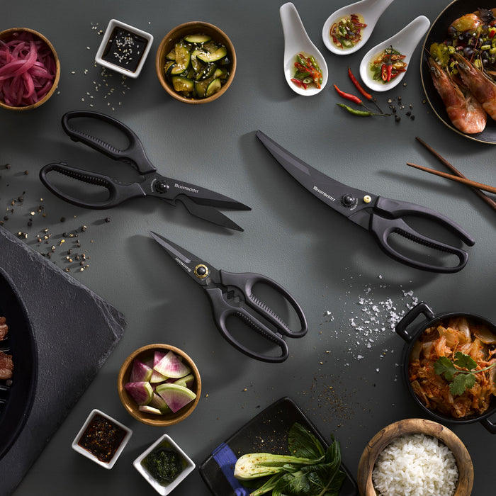 3 of the all black Messermeister Push Button Shear Collection on a dark gray surface with Korean BBQ dishes that have rice, shrimp, kimchi, pickled onions and spices