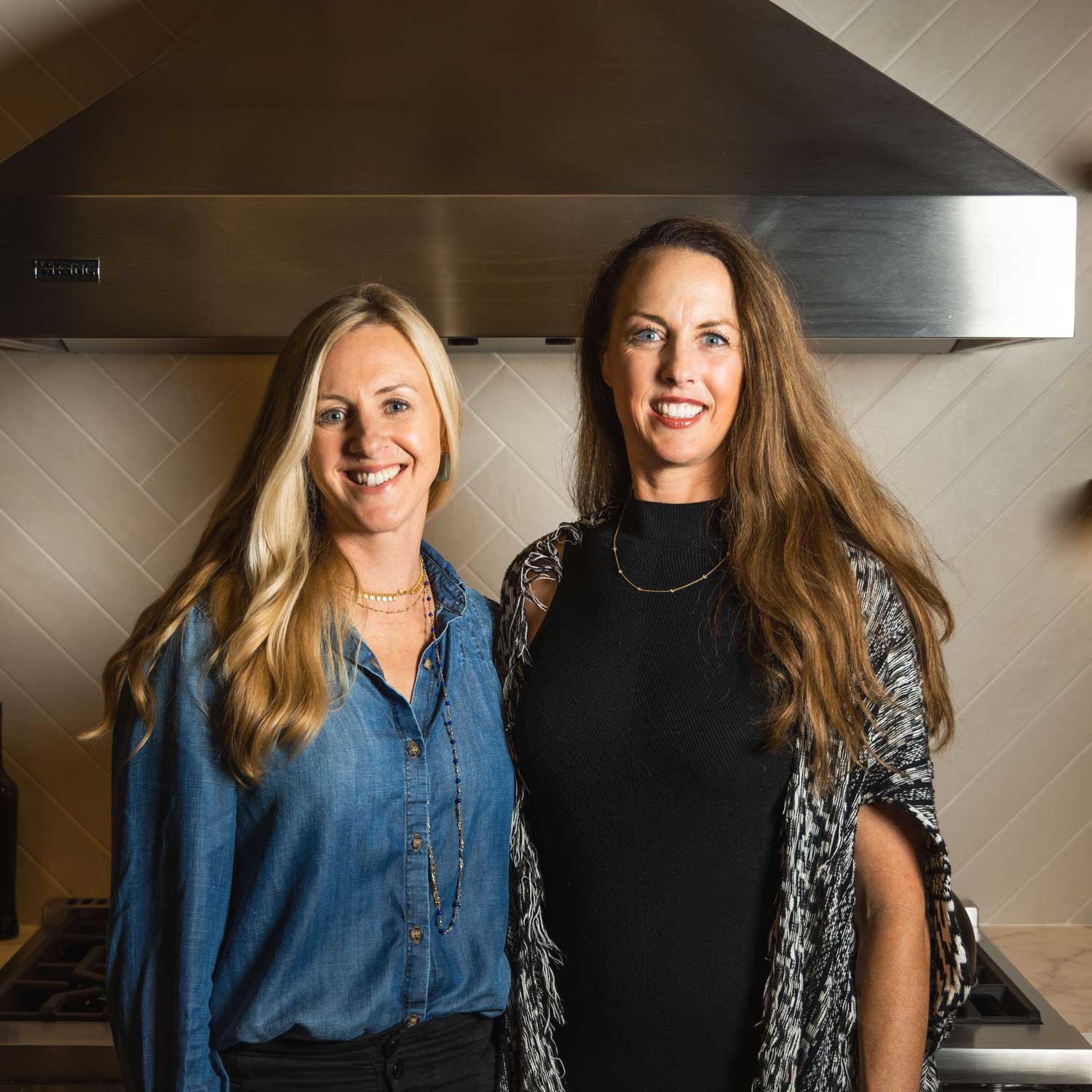 Messermeister Sisters, Kirsten and Chelcea Dressler, standing in a kitchen with a stainless steel range hood above them.
