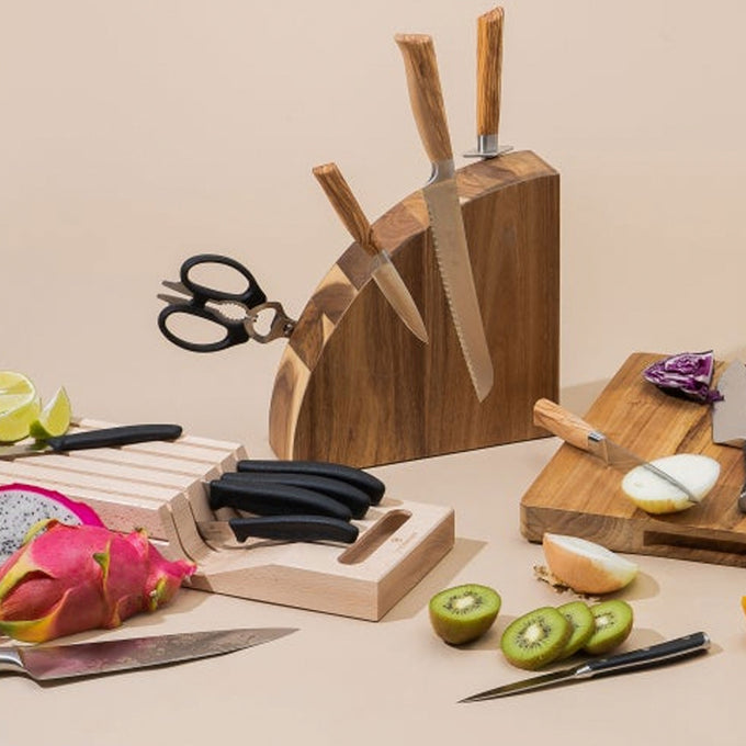 Set of knives in a wooden block with cutting boards and fruits on a beige background