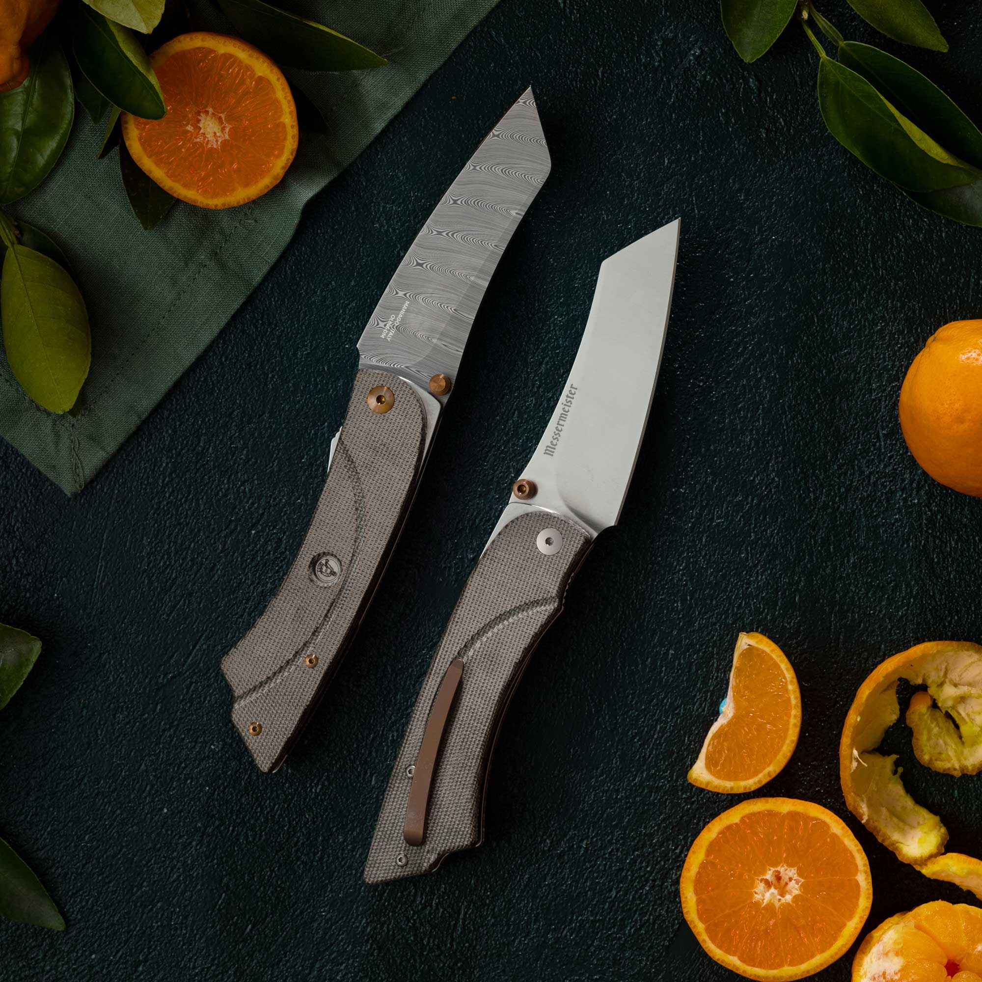 Messermeister Ojai Damasteel Folder - 3.75" - Made in Italy - OD Linen Micarta Handle - Damasteel SDT Steel and non damascus folder next to each other surrounded by oranges