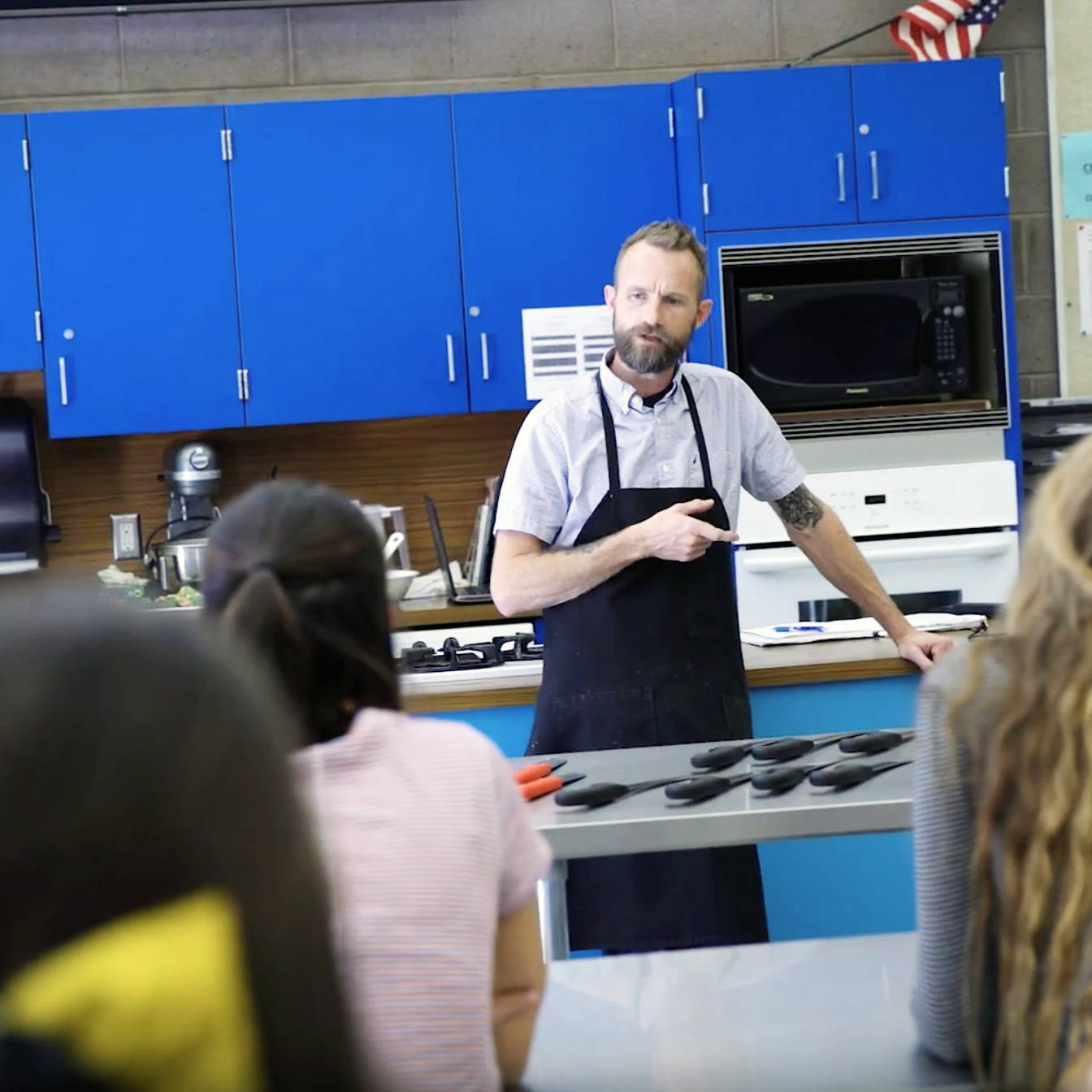 Teacher in a classroom setting with students and kitchen equipment.