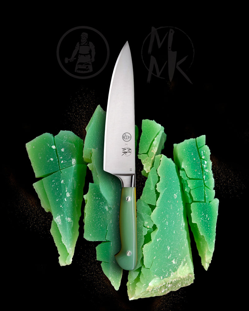 A high-end chef's knife with a polished silver blade and a translucent green handle, presented vertically amidst vibrant green crystalline shards on a solid black background. The 'MK' logo is visible on both the blade and as a stylized watermark in the background.