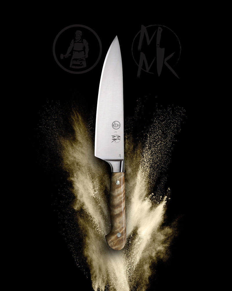 A professional chef's knife with a silver stainless steel blade and a brown marbled wood handle, shown vertically against a black background with a gold powder explosion effect. The brand logo 'MK' is visible on the blade.