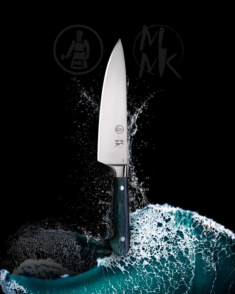 A professional chef's knife with a silver blade and a dark blue-green patterned handle, emerging from a splash of water against a solid black background. The brand logo 'MK' is visible on the blade, and stylized MK logos appear in the background.