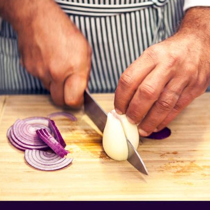 Person slicing onions on a wooden cutting board with a striped apron.