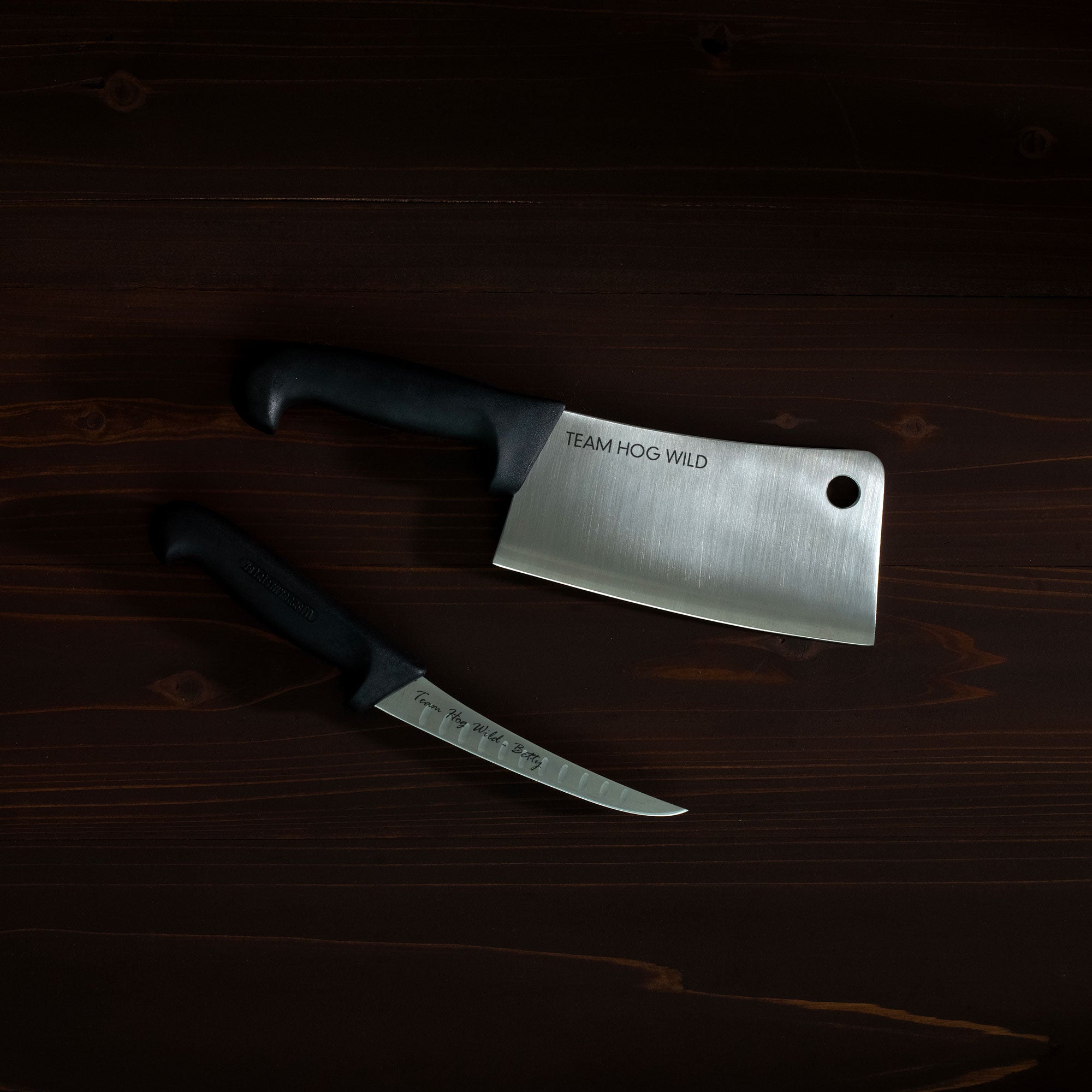Two knives on a wooden surface with 'Team Hog Wild' branding.