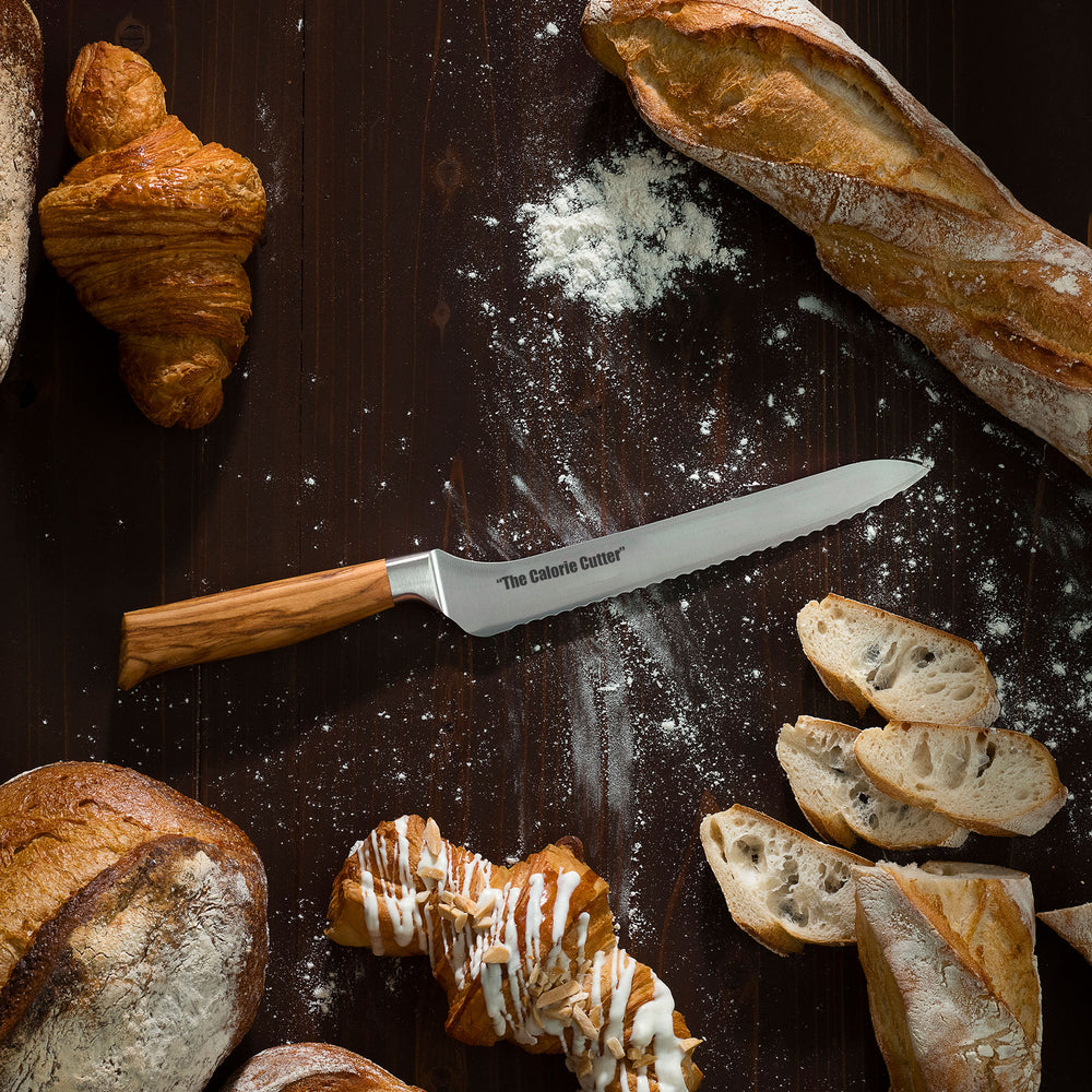 Knife labeled 'The Calorie Cutter' surrounded by various bread items on a dark surface with flour.