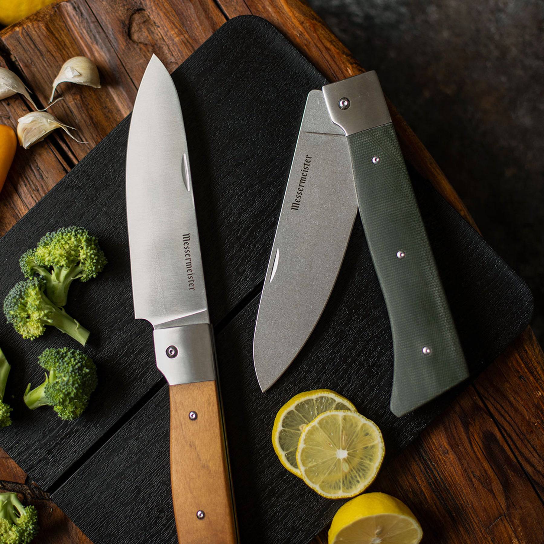 Messermeister Adventure Chef Folding 6 inch Chef's Knife with Maple handle shown fully extended lying on the Adventure Chef folding cutting board next to the Linen chef's knife with sliced fruits and vegetables