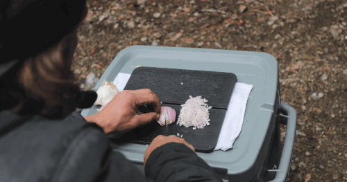 Video of a person at a campsite using the Adventure Chef 6 inch Chef's Knife to slice a shallot on a cutting board sitting on top of a cooler 