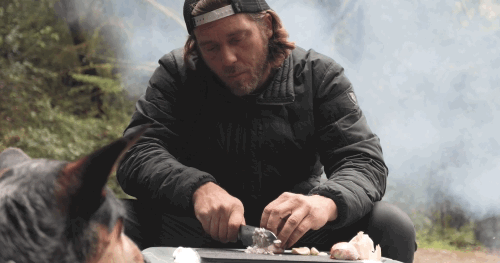 Video of a person at a campsite using the Adventure Chef 6 inch Chef's Knife to slice a shallot on a cutting board sitting on top of a cooler with a dog watching from the side 