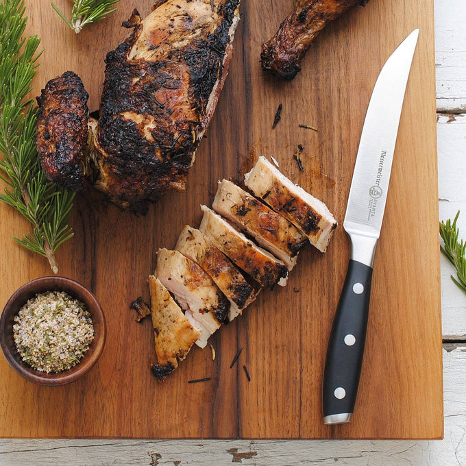 Messermeister Avanta 4-piece steak knife set with black POM handles next to cut chicken on wooden cutting board