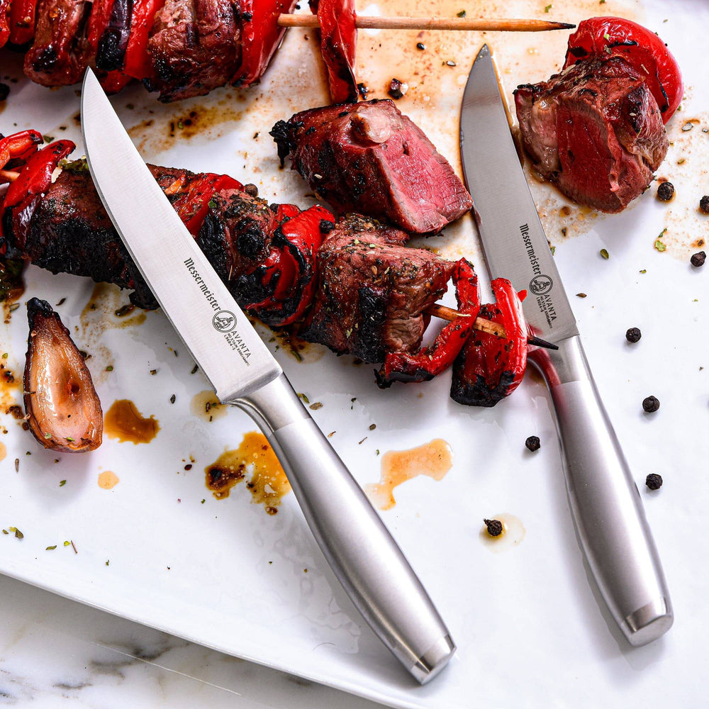 Messermeister Avanta steak knives with stainless steel handles resting on kabob skewer with meat and vegetables