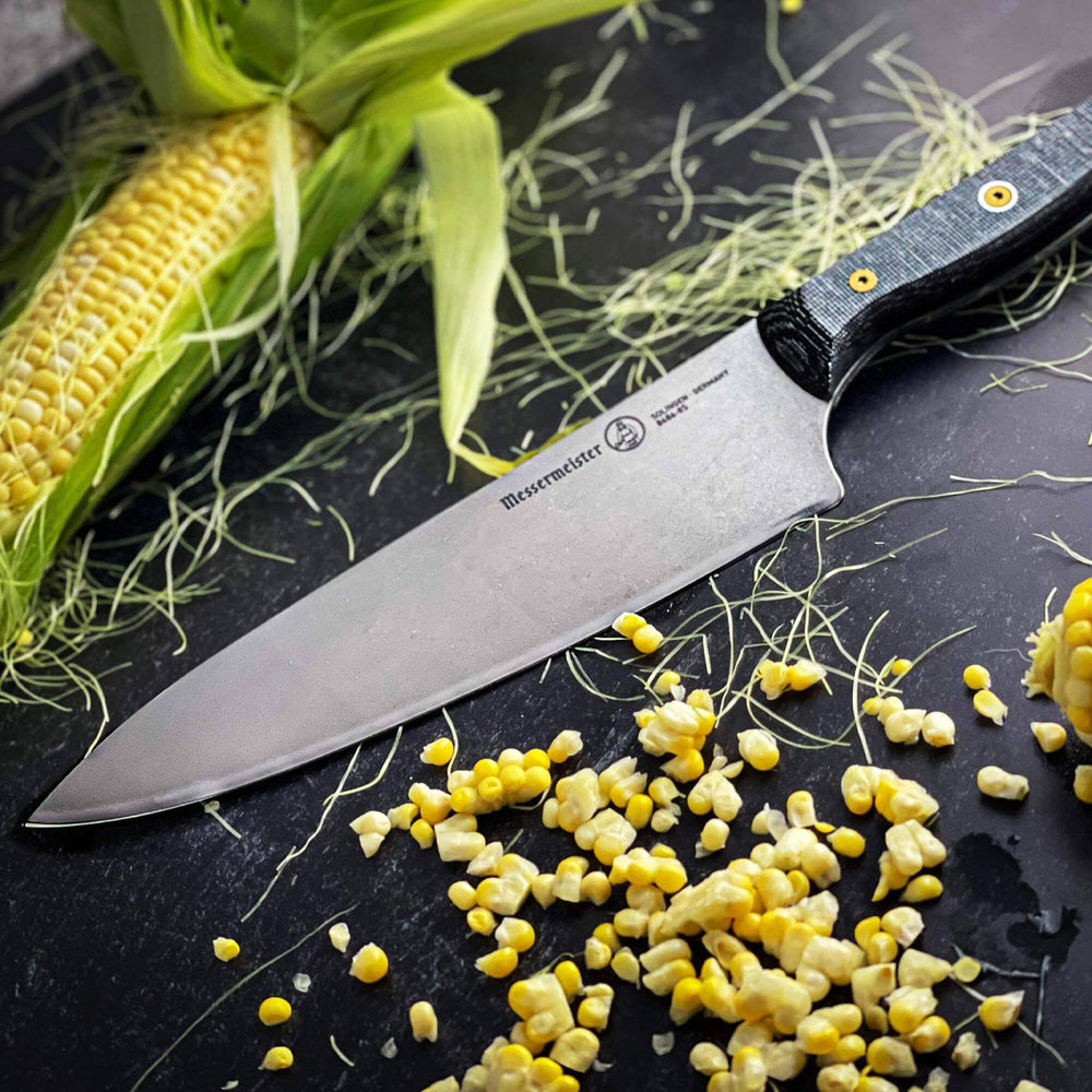 Messermeister custom chef’s knife on black table surrounded by fresh corn