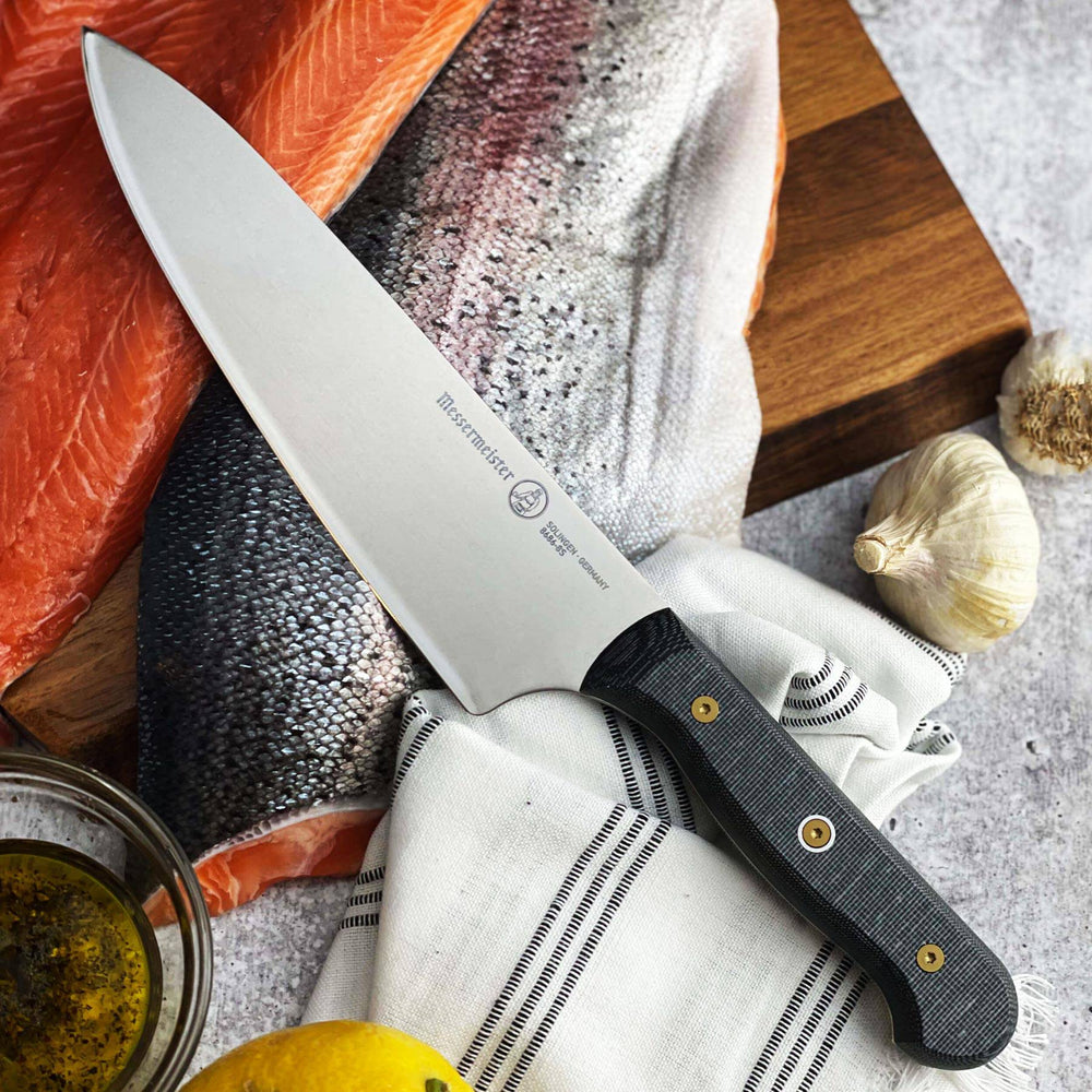 Messermeister Custom Chef’s knife on raw salmon fillet with garlic cloves and oil for food preparation