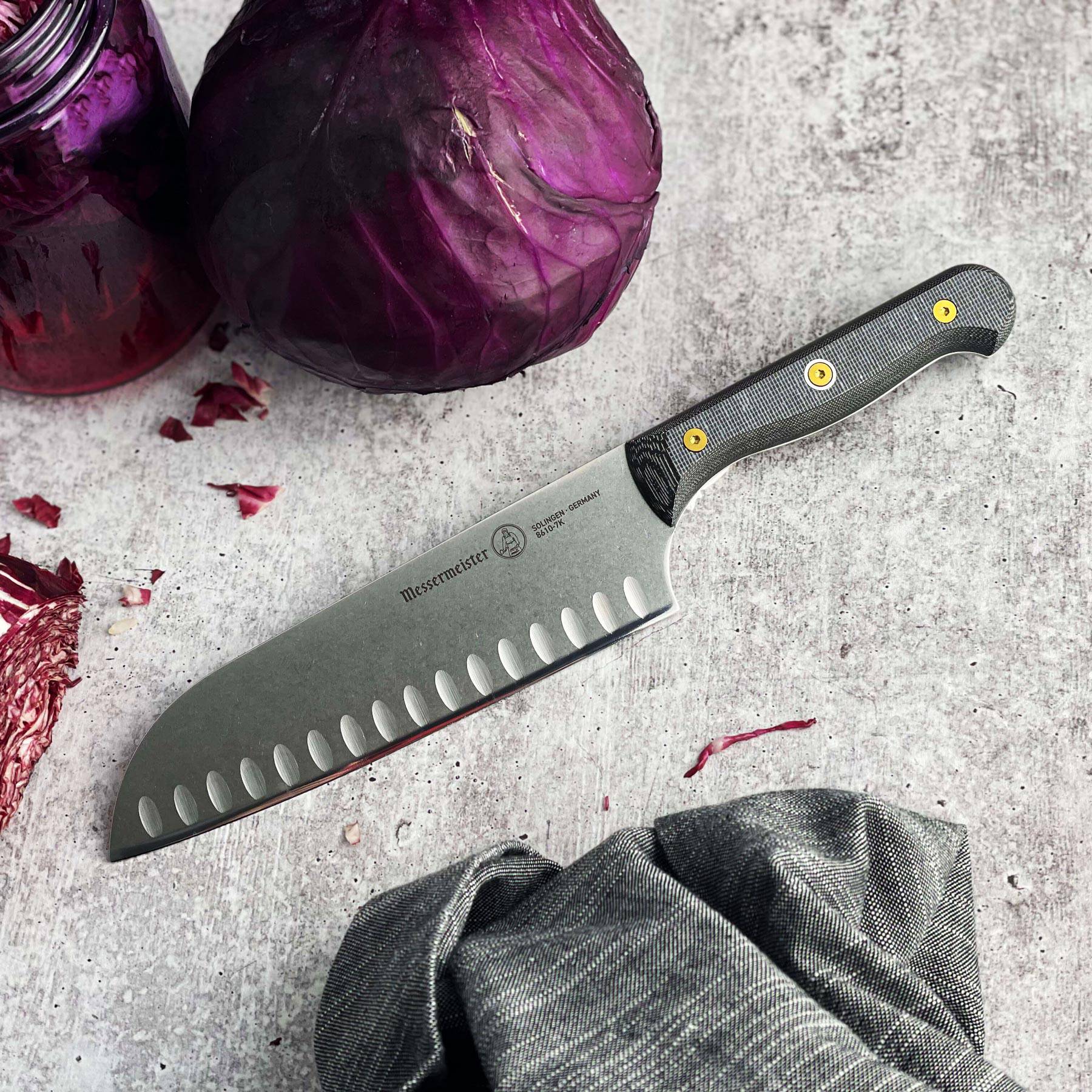 Messermeister Custom santoku knife resting on gray table surrounded by purple cabbage for kitchen prep