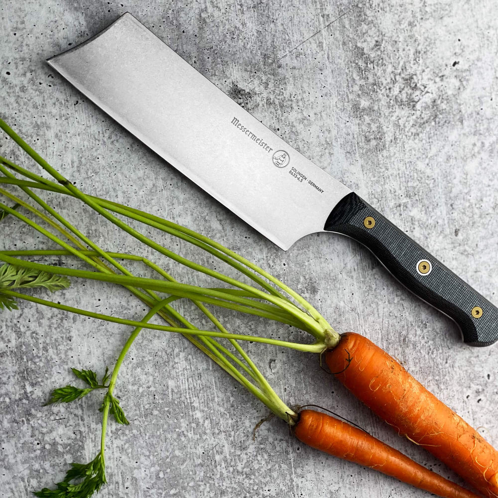 Messermeister custom nakiri knife displayed on gray surface with carrots for vegetable prep