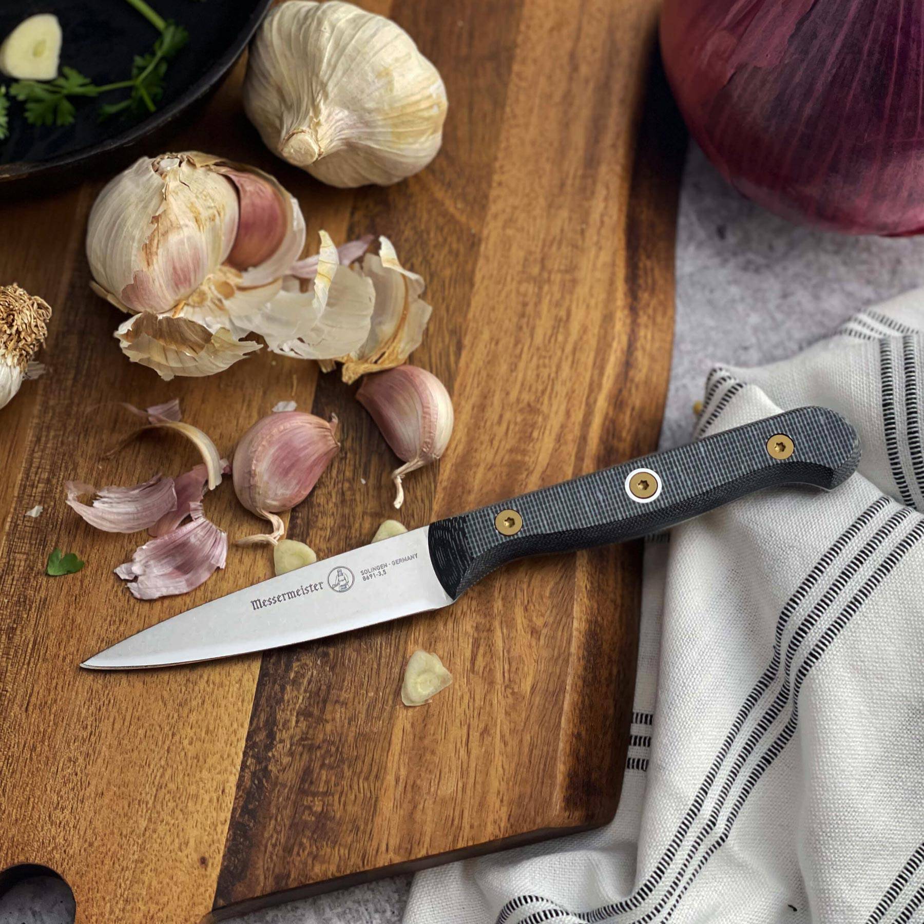 Messermeister Custom Paring Knife 3.5-inch resting on wood cutting board beside garlic cloves during kitchen preparation
