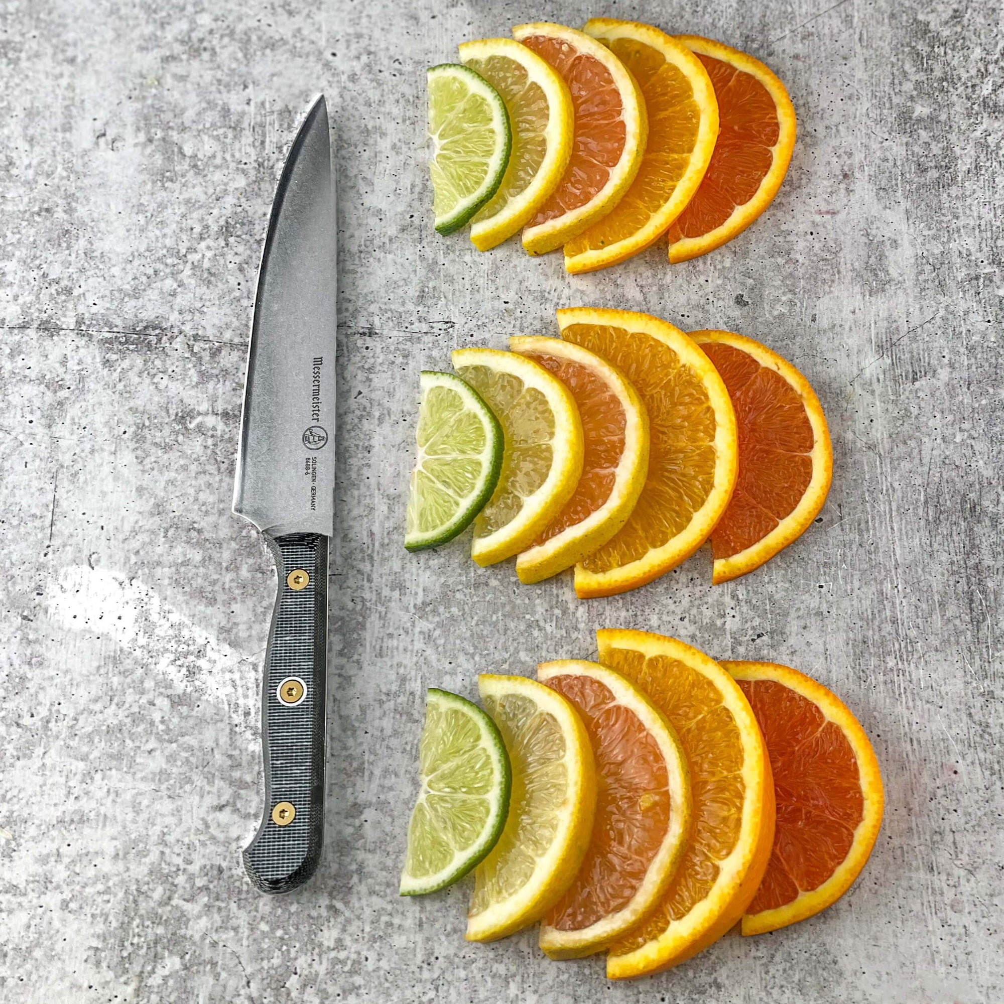 Messermeister Custom 6-inch utility knife next to neatly lined citrus wedges on a gray table