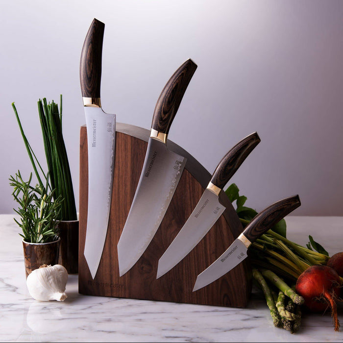 Messermeister Kawashima 5 Piece Magnet Block Set with the 10 inch slicer, 8 inch chef's knife, 6 inch utility knife, and 3.5 inch paring knife on a quarter round magnetic block shown sitting on a marble countertop surrounded by various vegetables 