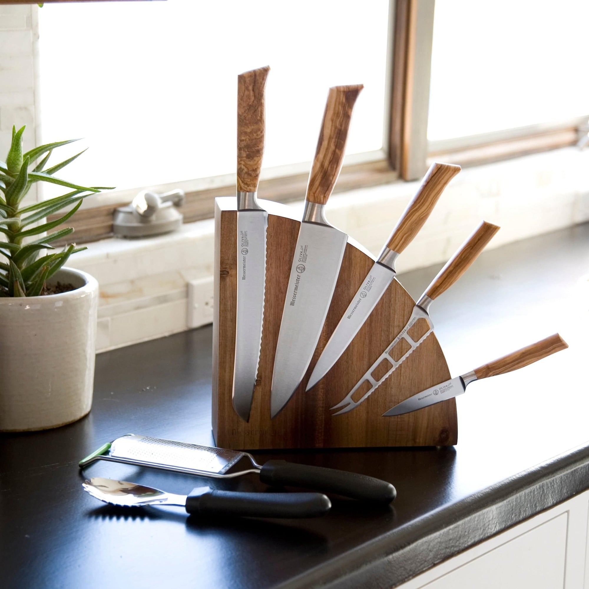 The Messermeister Quarter moon magnetic wooden block with 5 Olive wood handled knives attached. Resting on a black counter in a kitchen sitting.
