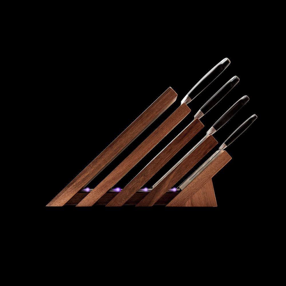Messermeister Next Level Magnetic Knife Block and UV light with a single black handled knife stored on each of the 4 slots. Block is showing the side view with handles to the right on a black background.