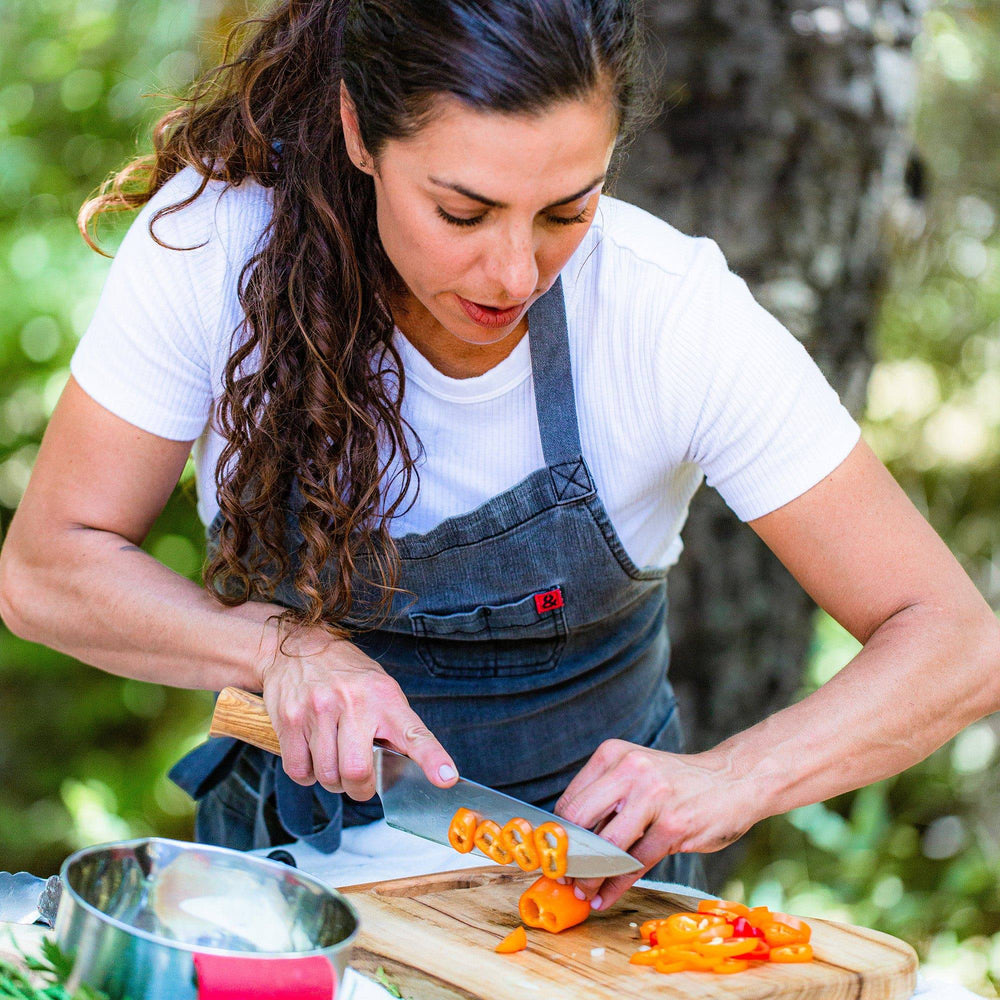 Photo of woman wearing a denim apron slicing yellow peppers with Oliva Elite chef's knife on a cutting board