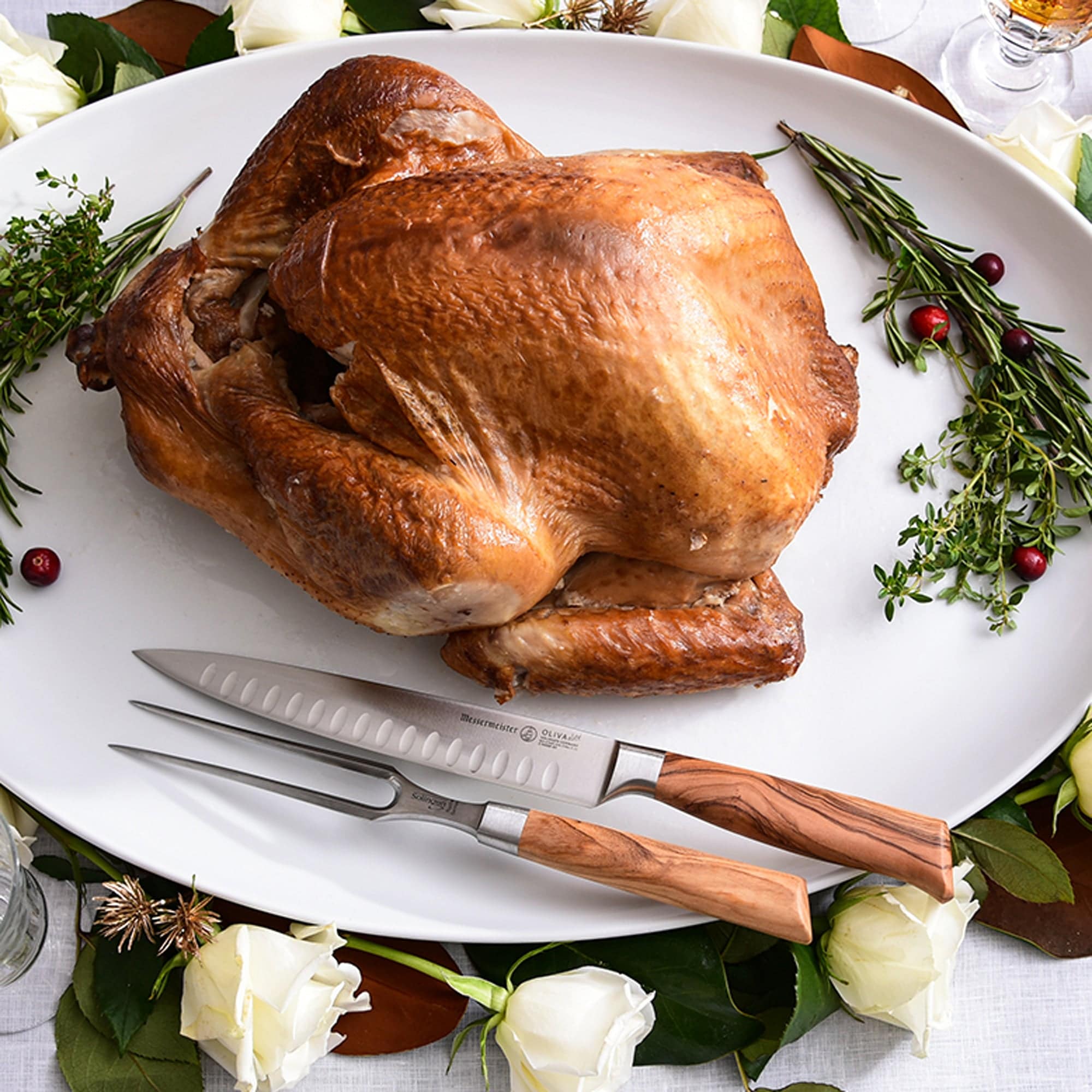 The Oliva Elite Kullens Carving Set shown resting next to a roast turkey on a large platter with herbs and flowers