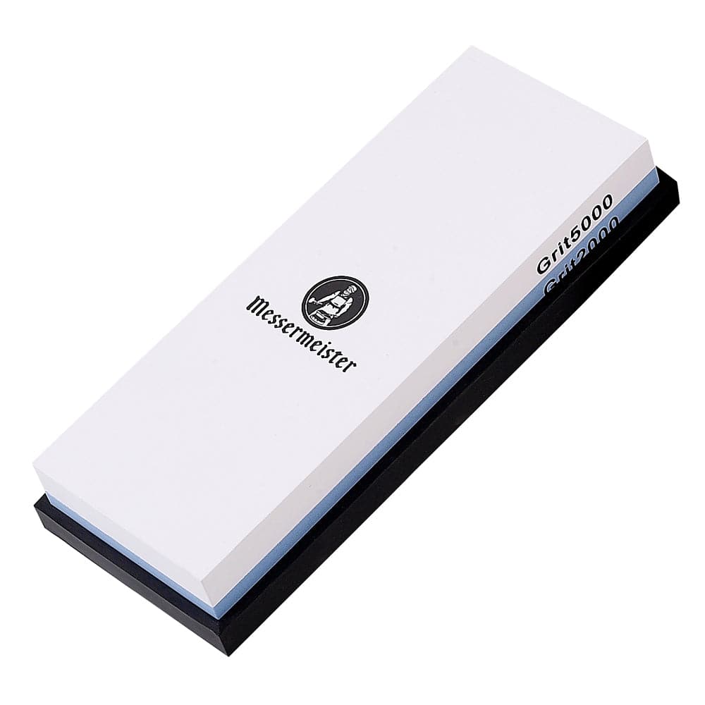 Messermeister  2000 & 5000 Grit Polishing Stone is a dual sided rectangle 8 inch x 3 inch x 1 inch. The top layer is white with black "Messermeister" logo. "Grit5000" labeled in black along the edge.  Bottom layer is blue with "Grit2000" labeled along edge. The item sits in a rectangular black silicone base. Image tilted up and to the right on a white background.