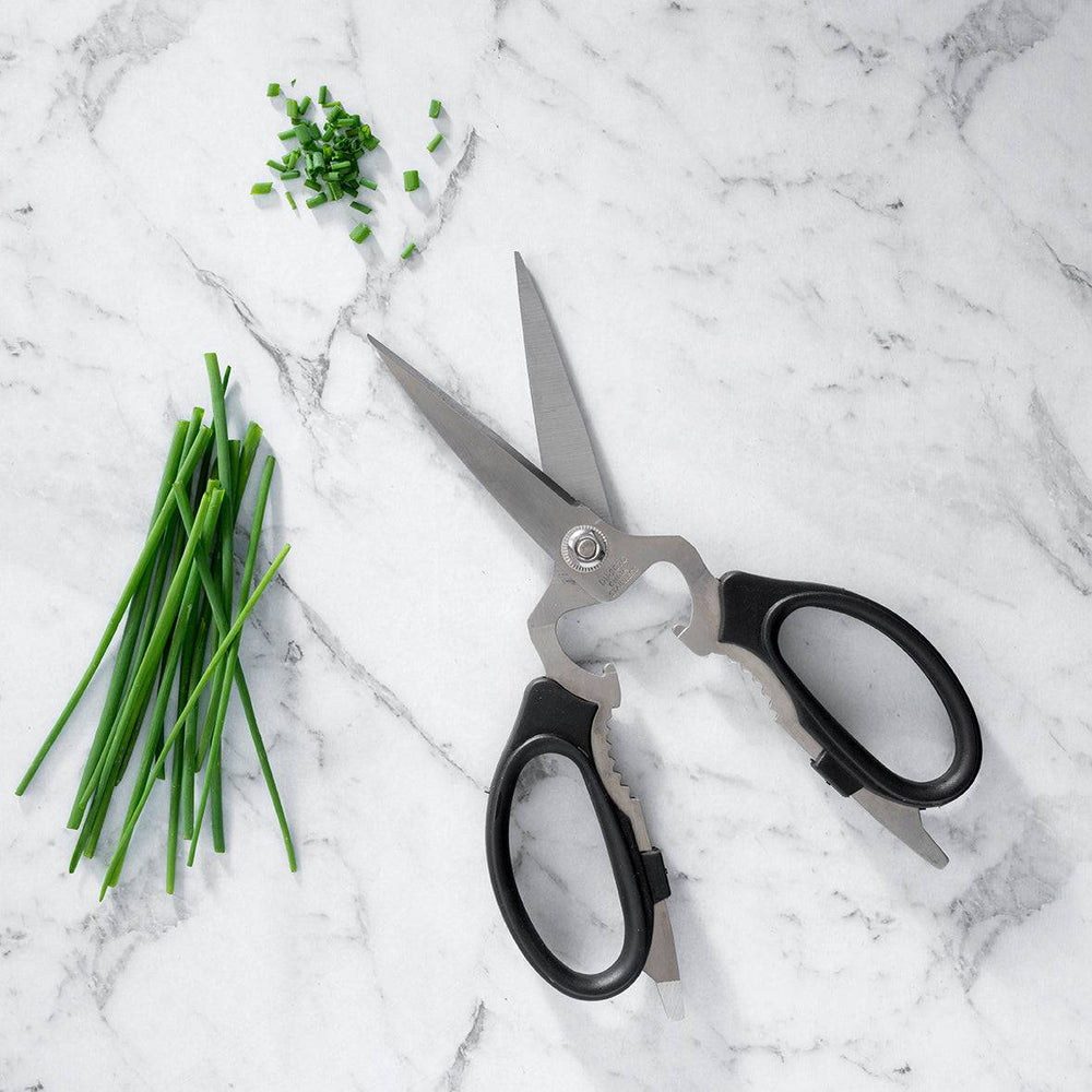 Messermeister take-apart kitchen scissors with stainless steel blades and ergonomic handles, displayed next to fresh chives on a marble table, showcasing precision cutting and easy-clean detachable design for kitchen prep