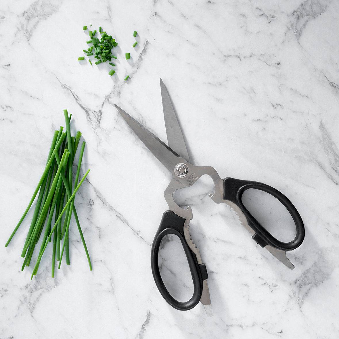 Messermeister take-apart kitchen scissors with stainless steel blades and ergonomic handles, displayed next to fresh chives on a marble table, showcasing precision cutting and easy-clean detachable design for kitchen prep