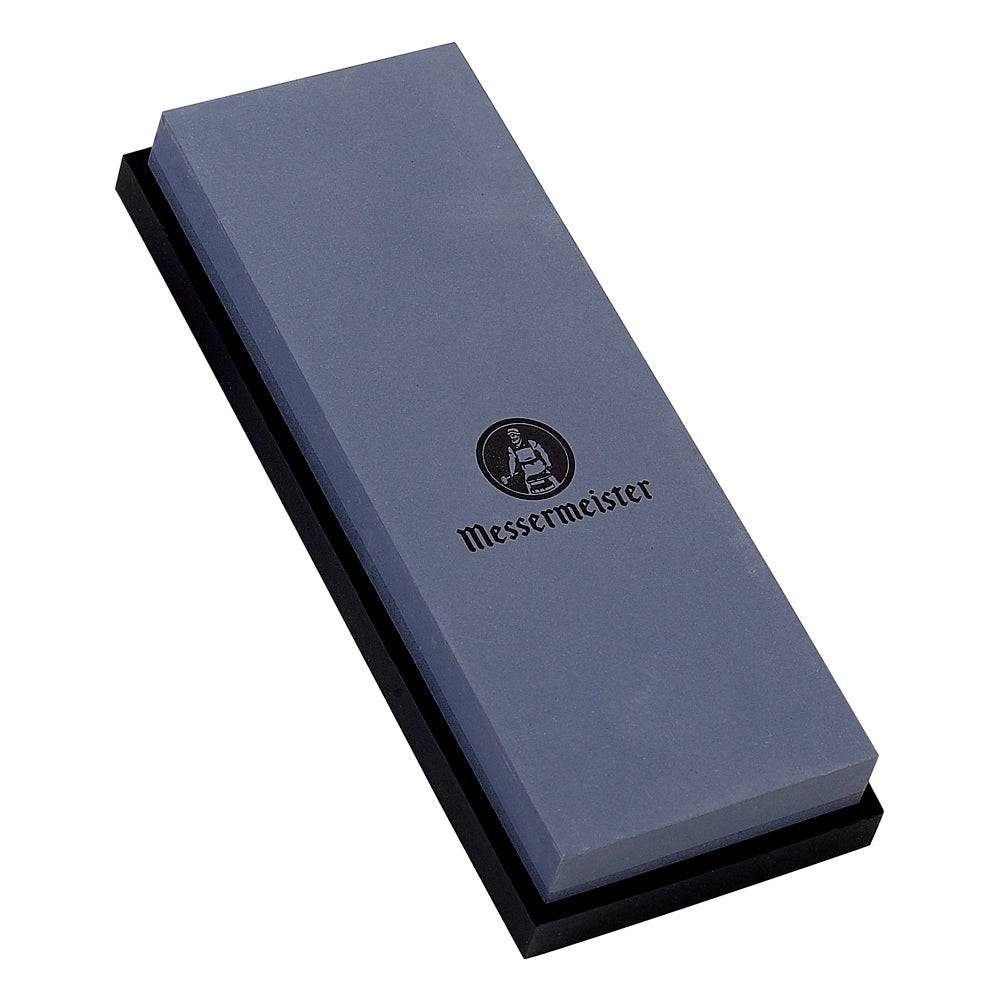 Messermeister 400 & 1000 grit Restoration Stone  is a dual sided rectangle. The top layer is gray with black "Messermeister" logo.  Bottom layer is black. The item sits in a rectangular black silicone base. Image tilted up and to the left on a white background.  